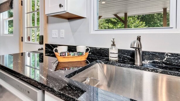A modern kitchen with a stainless steel sink, a wooden coffee table with cups, and a window with a view of greenery. - Bear Walk Cottage in Black Mountain (Black Mountain)