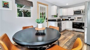 A modern kitchen with white cabinets, stainless steel appliances, and a round dining table with chairs. - Bear Walk Cottage in Black Mountain (Black Mountain)