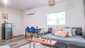A modern living room with a grey sofa, a wooden coffee table, and a dining area with blue chairs. - NEW Designed Apt 2023 NrUCF PETSOk PrivateEntry (Orlando)