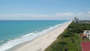 A beach with a clear view of the ocean, a sandy shore, and a few buildings in the distance. - NEW Designed Apt 2023 NrUCF PETSOk PrivateEntry (Orlando)