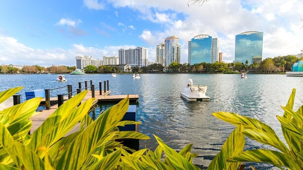 A waterfront view with a dock, a swan, and modern buildings in the background. - NEW Designed Apt 2023 NrUCF PETSOk PrivateEntry (Orlando)