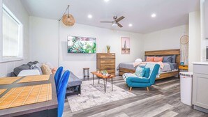 A modern, well-lit room with a bed, a blue armchair, a wooden dresser, and a dining area with a table and chairs. - NEW Designed Apt 2023 NrUCF PETSOk PrivateEntry (Orlando)