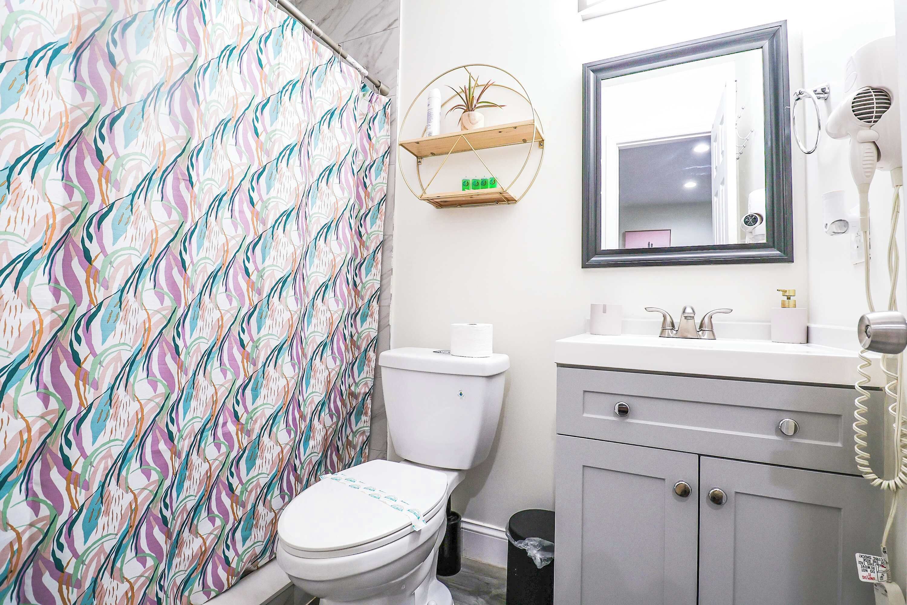 Un baño con inodoro, lavamanos, espejo y secador de pelo.