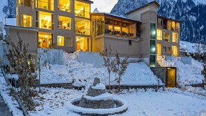 Un hotel moderno con varios pisos, grandes ventanales y un paisaje nevado con montañas al fondo.