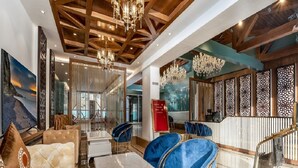 Un vestíbulo espacioso con techo alto, vigas de madera y candelabros. Hay áreas de descanso con sofás y sillones cómodos, y un mostrador de recepción con paneles decorativos.