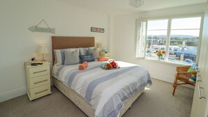 A bedroom with a bed, bedside tables, a dresser, a window with a view, and a chandelier.