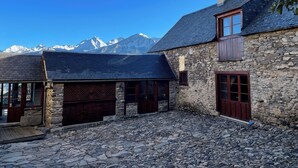 Un edificio de piedra con techo inclinado y puertas de madera, con montañas nevadas al fondo.