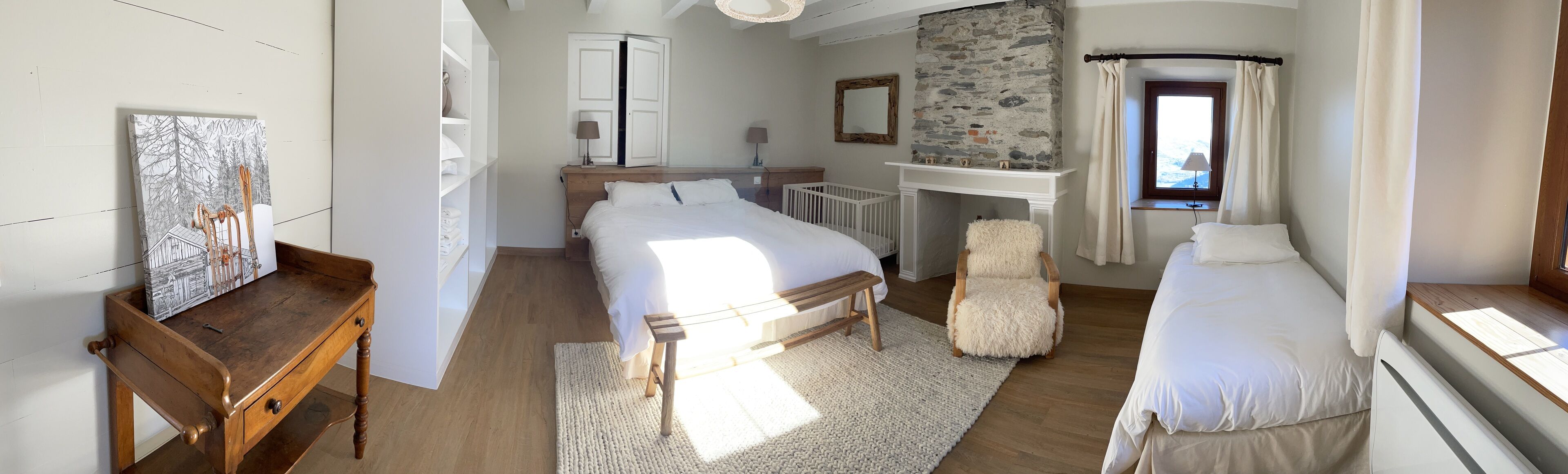 Un dormitorio con una cama grande, una cama más pequeña, una silla de madera, un tocador blanco, un espejo y una chimenea.