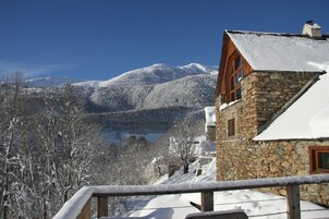 Un edificio de piedra con un balcón de madera, árboles cubiertos de nieve y una montaña al fondo.