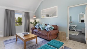 A living room with a brown leather sofa, a wooden coffee table, and a teal ottoman. - Winelands Golf Lodges 40 (Stellenbosch)