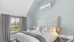 A bedroom with a large bed, a bedside table with a lamp, a window with curtains, and an air conditioning unit on the wall. - Winelands Golf Lodges 40 (Stellenbosch)