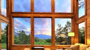A room with large windows offering a view of a forest and mountains. - 🐻Gatlinburg Mountain Romance: Secluded, Honeymoon, Outdoor Fireplace, Hot Tub🏞 (Gatlinburg)