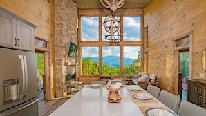 A spacious wooden interior with a large dining table, stone fireplace, and a scenic mountain view through large windows. - 🐻Gatlinburg Mountain Romance: Secluded, Honeymoon, Outdoor Fireplace, Hot Tub🏞 (Gatlinburg)