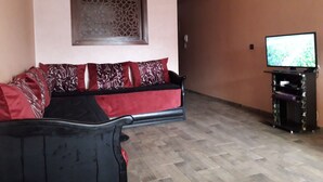 Una sala de estar con un sofá, un televisor sobre un mueble bajo y un ventanal con diseño.