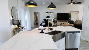 A modern kitchen with a central island, stainless steel dishwasher, and pendant lighting.