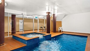 Ein Innenpool mit separatem Whirlpoolbereich, Glastüren und einer Sitzecke mit Stühlen.