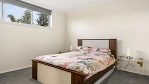 Ein Schlafzimmer mit einem Bett, einem Fenster, einem Nachttisch und einer Lampe.