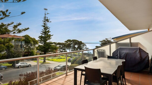 Ein Balkon mit Tisch und Stühlen mit Blick auf eine Straße und Grünflächen.