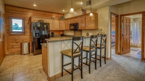 A kitchen with wooden cabinets, a stainless steel refrigerator, a microwave, and a granite countertop. There are three bar stools and a trash can. - Cozy Golf course condo with A/C (pagosa springs)