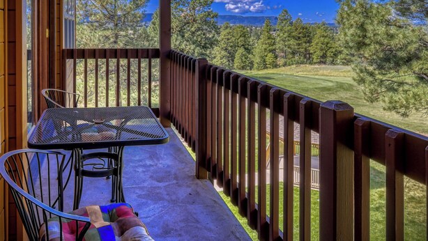 A balcony with a table and chairs, a wooden railing, and a view of a golf course. - Cozy Golf course condo with A/C (pagosa springs)