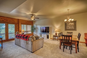 A cozy living room with a sofa, a dining table, and chairs, a ceiling fan, and a TV in the background.