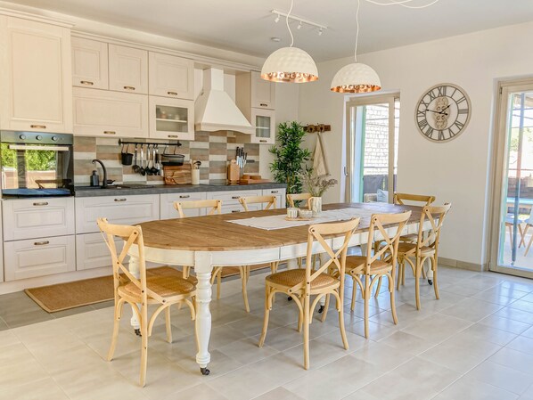 A modern kitchen with white cabinetry, a wooden dining table, and pendant lights.
