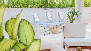 Un espace extérieur ensoleillé, aménagé avec des fauteuils confortables et une petite table, le tout entouré de verdure.