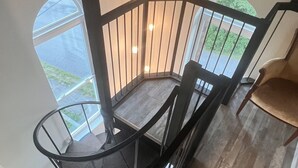Una escalera moderna con barandilla de vidrio que da a un balcón con vistas al exterior.
