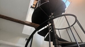 Una escalera en espiral con barandilla de metal, viga de madera y lámpara colgante.