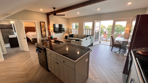 Amplia sala de estar con isla de cocina, comedor y balcón con mobiliario exterior.