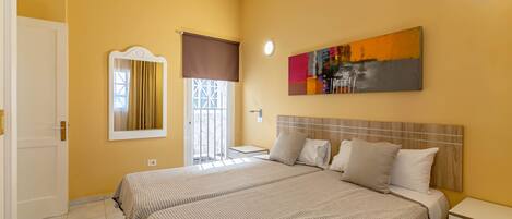 A hotel room with two beds, a large window with curtains, a painting on the wall, and a bedside table.