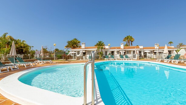A swimming pool with lounge chairs and umbrellas, surrounded by palm trees and a clear blue sky. - Vista Verde Adult Only (San Bartolomé de Tirajana)