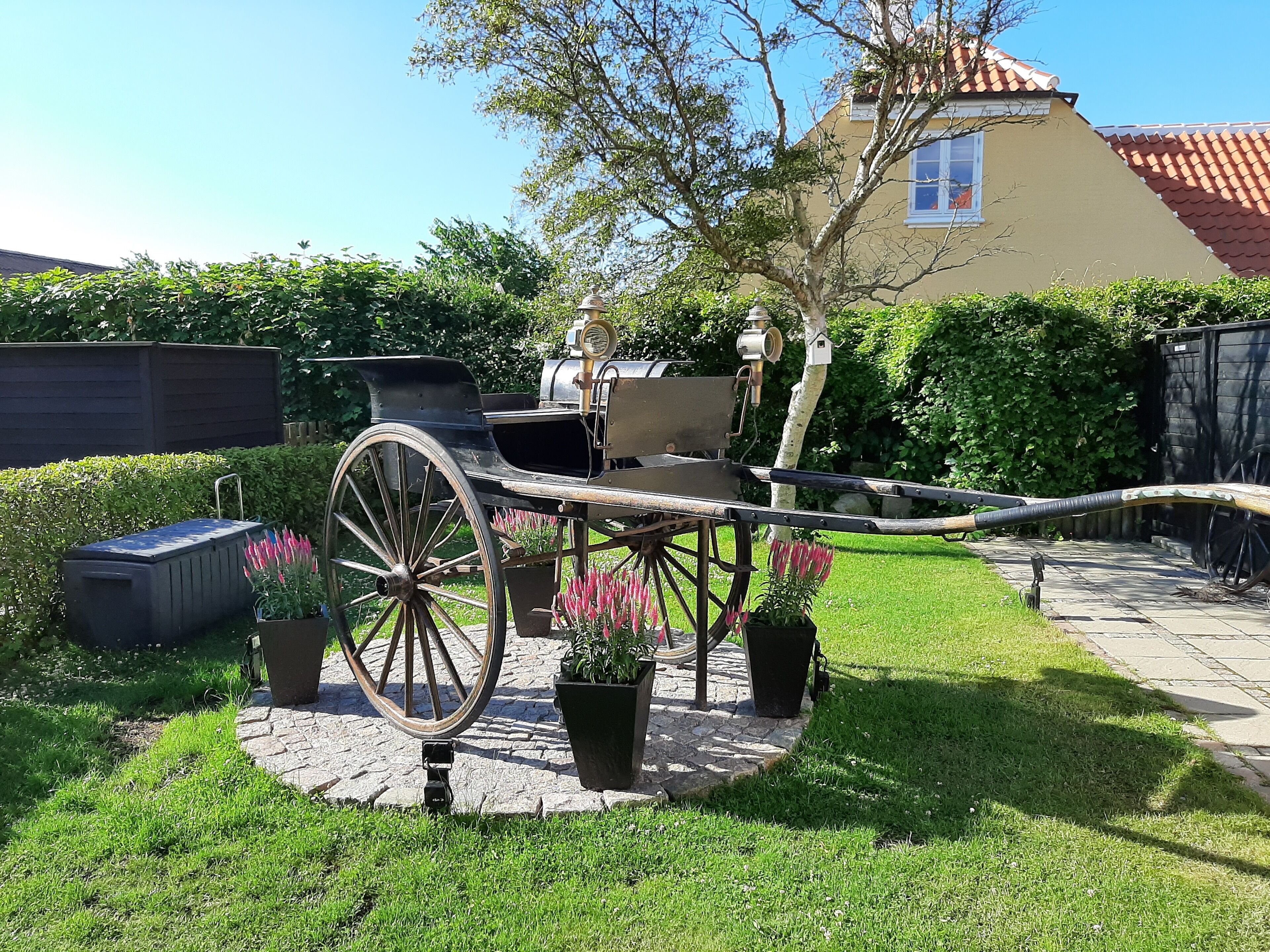 A vintage carriage parked in a garden with a house in the background.