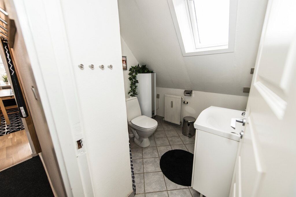 Een compacte, moderne badkamer met een wit toilet, een klein wastafeltje en een radiator.