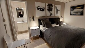 Un dormitorio con cama, mesitas de noche, una silla y obras de arte en las paredes.