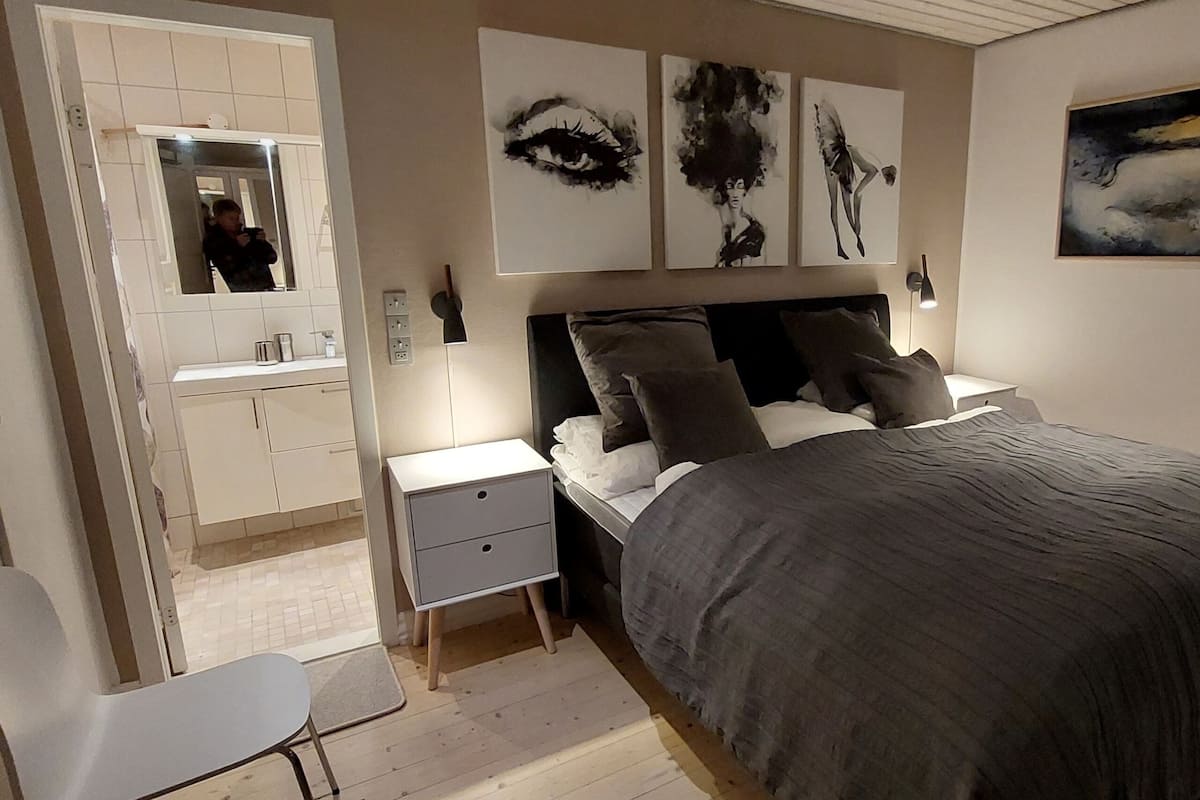 A bedroom with a bed, bedside tables, a chair, and artwork on the walls.