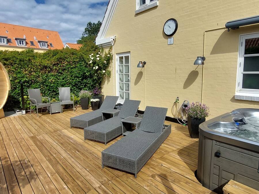 A wooden deck with lounge chairs, a hot tub, and a sauna.