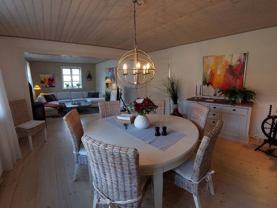 A dining area with a round table, wicker chairs, a chandelier, and a painting on the wall.