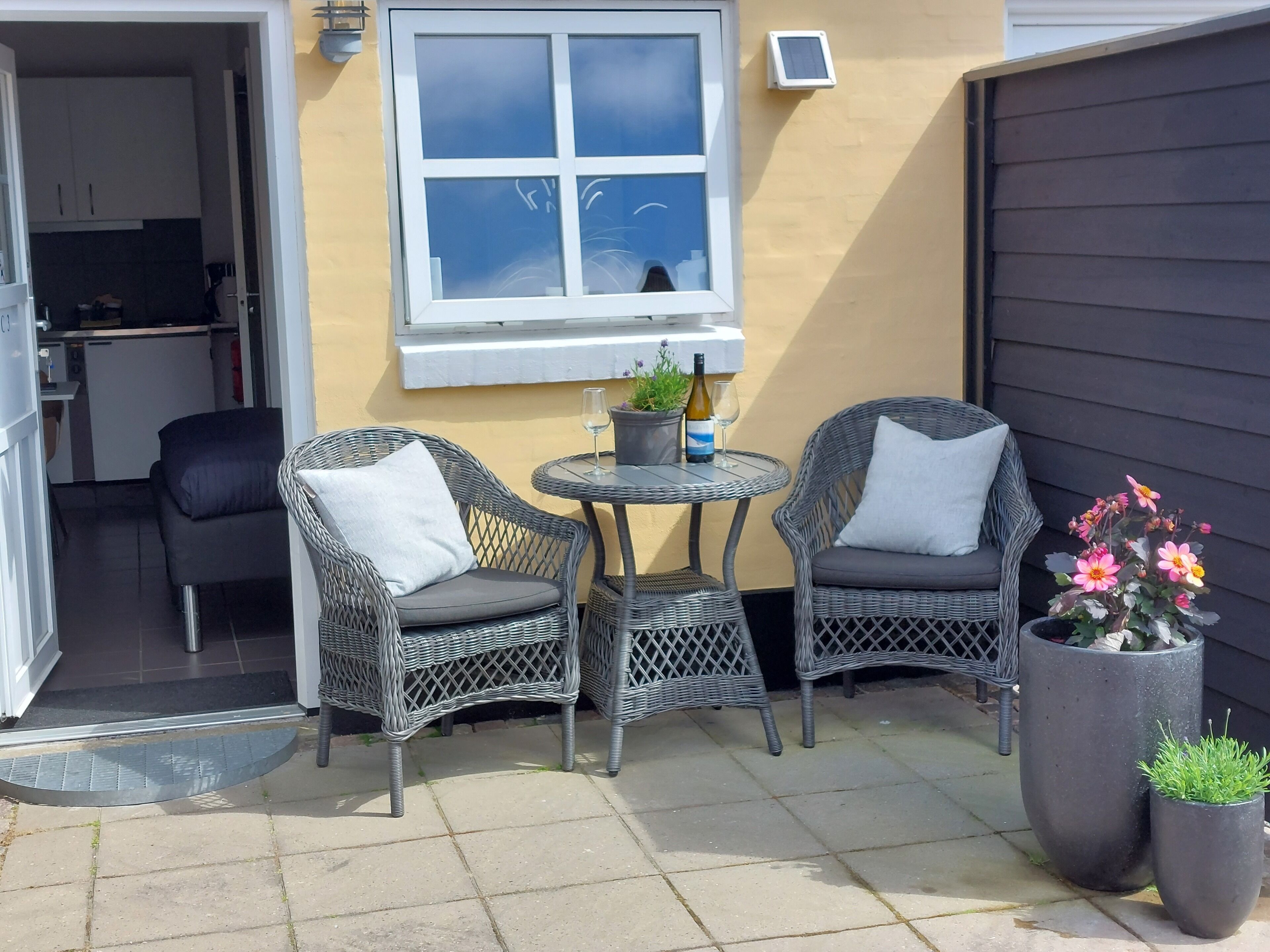 A patio with two wicker chairs, a small round table, and a potted plant.