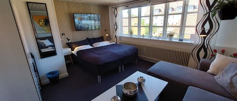 Une chambre d’hôtel moderne dotée d’un grand lit, d’un canapé, d’une télévision et d’une fenêtre donnant sur des immeubles.
