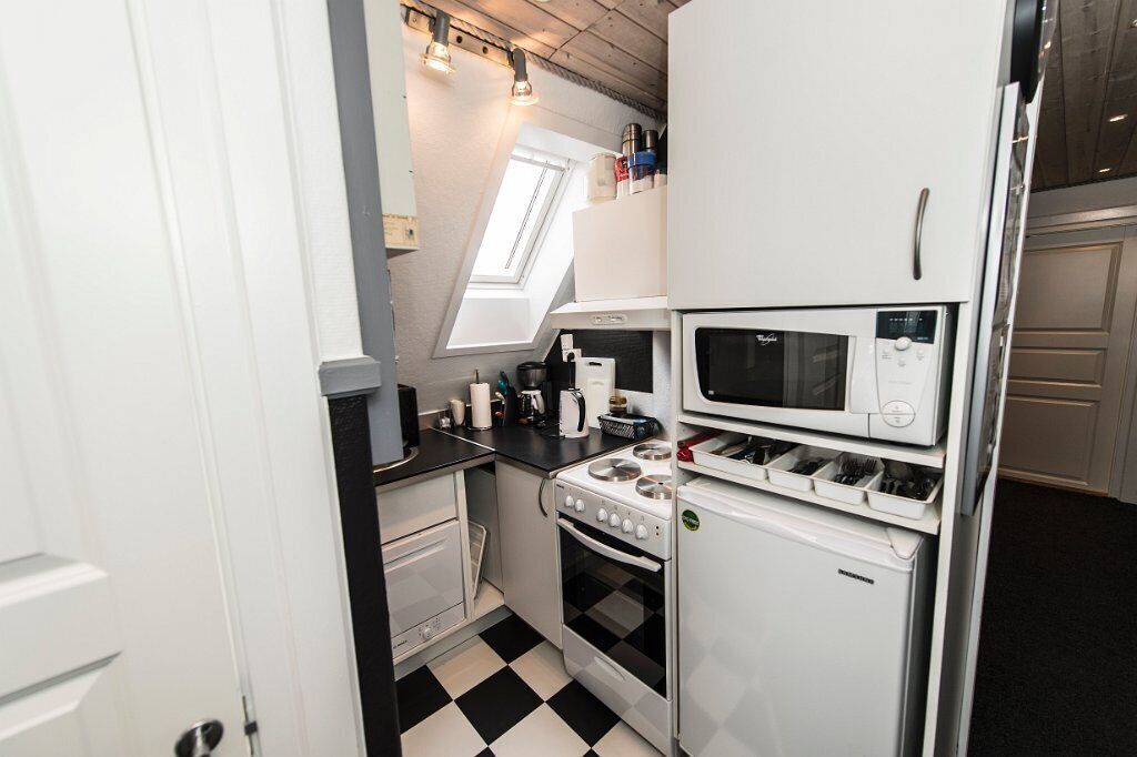 Een compacte keuken met een gasfornuis, magnetron en koelkast, met een geruit vloertje en een dakraam.