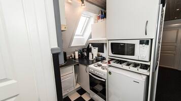 Een compacte keuken met een gasfornuis, magnetron en koelkast, met een geruit vloertje en een dakraam.