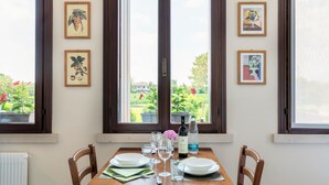 A dining table set with plates, glasses, and a bottle of wine, with a window view of greenery and houses.