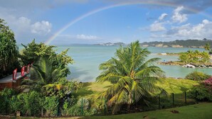 Una playa tropical con un arcoíris, exuberante vegetación y una vista despejada del océano.