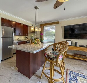 A modern kitchen with a central island, stainless steel appliances, and a dining area with a TV and wicker chairs.