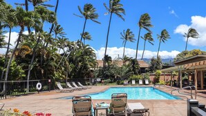 A pool area with lounge chairs and a covered seating area, surrounded by tall palm trees. - Serene Private Ocean View  AC  Pool (Lahaina)