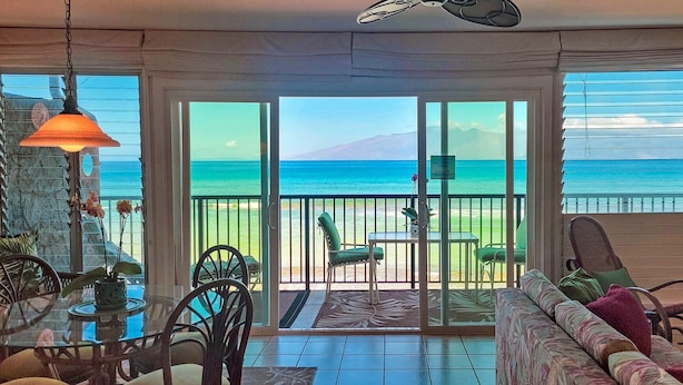 Une chambre avec vue sur l’océan, un balcon avec des fauteuils et un coin repas avec une table et des chaises.
