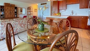 Un coin repas avec une table en verre entourée de chaises en bois, un ventilateur de plafond et des lampes suspendues.