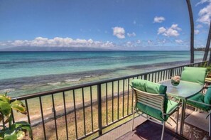 A balcony with a view of the ocean, green chairs, and a small table with a bowl. - 1 Bed $ for 2 bed Condo! Direct Ocean Views Pool (Lahaina)