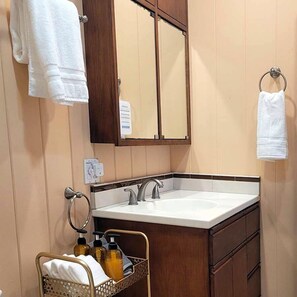 A bathroom with a sink, mirror, towel rack, and a basket with toiletries. - 1 Bed $ for 2 bed Condo! Direct Ocean Views Pool (Lahaina)
